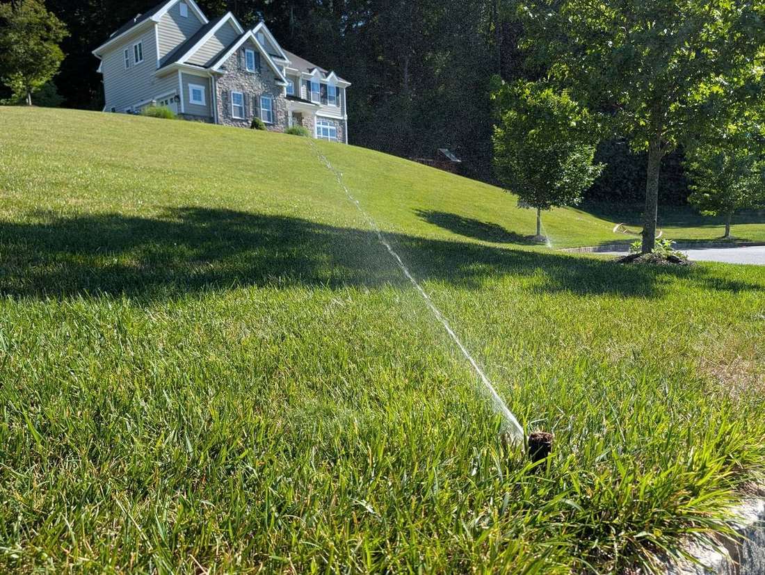 A lawn sprinkler spraying an arc of water across a healthy green lawn in front of a stone colonial home — JHL Irrigation system in Delaware County, PA